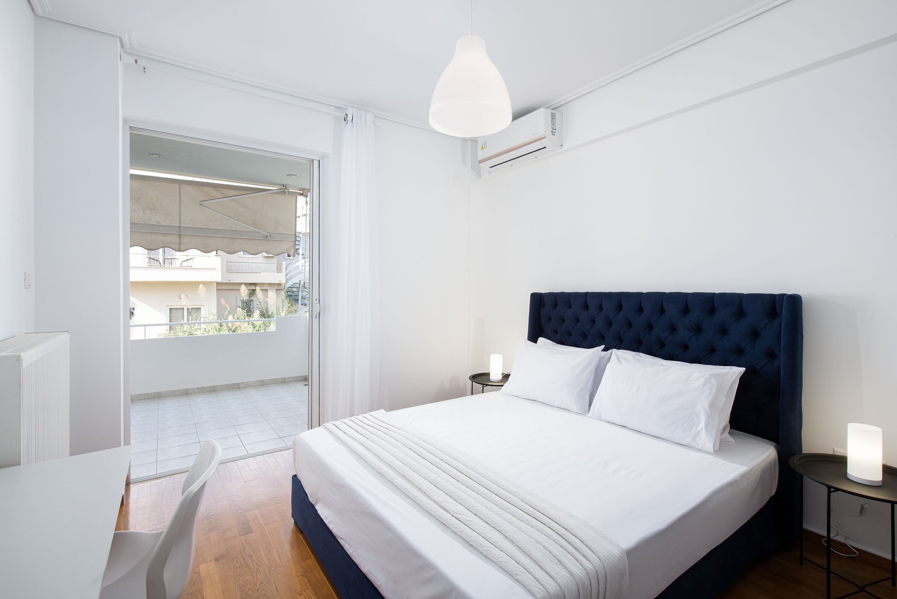 Une chambre avec un grand lit, une table de chevet avec une lampe et une vue sur le balcon extérieur.