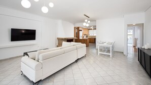 Ein modernes Wohnzimmer mit einem weißen Sofa, einem Flachbildfernseher und einem Essbereich mit Tisch und Stühlen.
