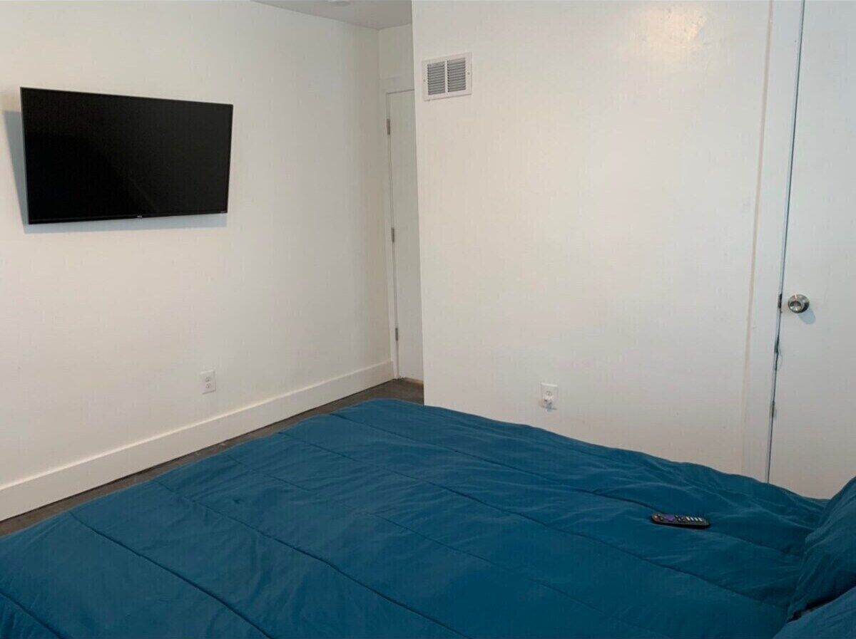 A room with a bed, a flat-screen TV mounted on the wall, and a door with a vent.