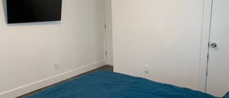 A room with a bed, a flat-screen TV mounted on the wall, and a door with a vent.