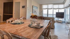 A dining area with a wooden table set for four, surrounded by upholstered chairs. A large window provides a view of the outdoors. - Phoenix Luxury Loft in Cádiz (Cádiz)