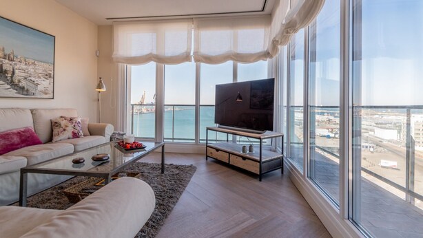 A modern living room with a sofa, coffee table, and TV, large windows with a view of the city and sea. - Phoenix Luxury Loft in Cádiz (Cádiz)