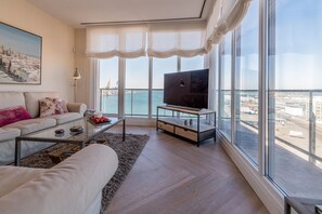 A modern living room with a sofa, coffee table, and TV, large windows with a view of the city and sea. - Phoenix Luxury Loft in Cádiz (Cádiz)