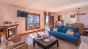 A living room with a fireplace, a blue sofa, wicker chairs, a coffee table, and a dining area with a table and chairs.