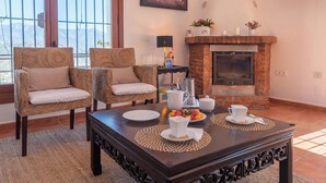 A cozy living room with wicker chairs, a dark wooden coffee table, and a fireplace.