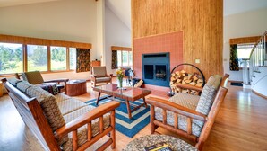 A spacious living room with a fireplace, wooden furniture, and large windows offering a view of the outdoors. - Wyoming Retreat on Wood River: Hike & Fly Fish! (Meeteetse)