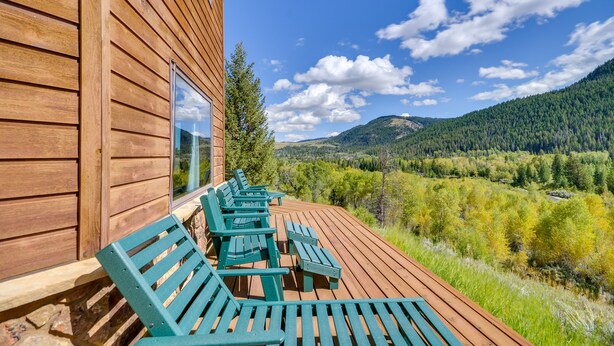 A wooden deck with outdoor seating and a view of a forested valley. - Wyoming Retreat on Wood River: Hike & Fly Fish! (Meeteetse)