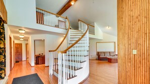 A spacious interior with a curved staircase, wooden flooring, and a large wooden panel on one wall. - Wyoming Retreat on Wood River: Hike & Fly Fish! (Meeteetse)