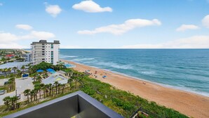 A beach view with a hotel building, palm trees, and a clear sky.