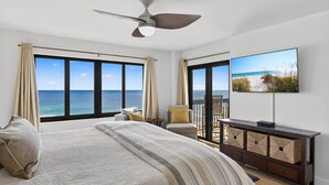 A bedroom with a large bed, a ceiling fan, a TV, and a view of the ocean.