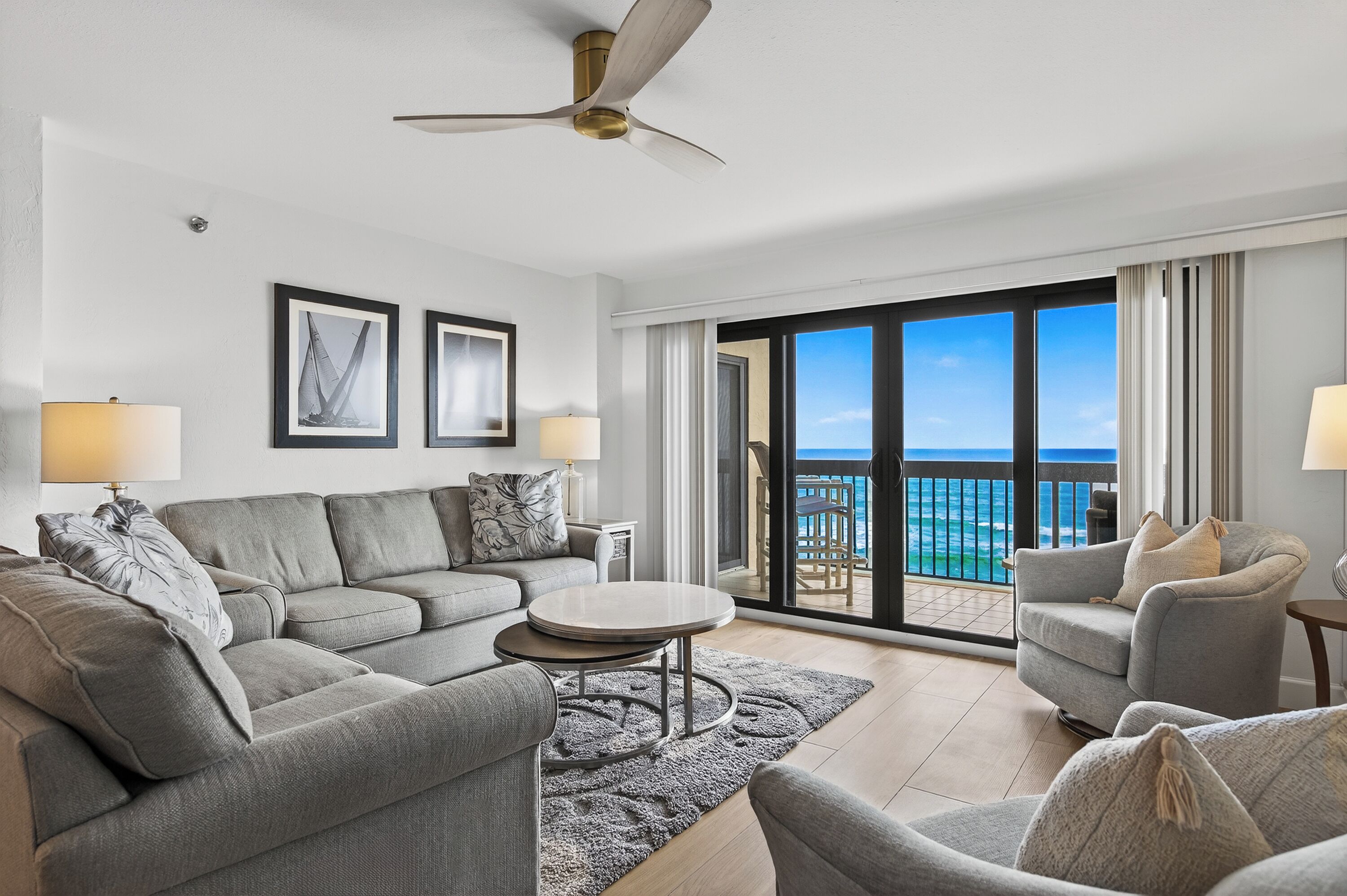 A modern living room with a sofa set, a coffee table, and a view of the ocean through large windows.