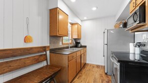 A compact kitchen with wooden cabinets, a built-in bench, a stainless steel refrigerator, and a microwave on an elevated shelf. - 2BR Duplex Cabin w/Community Pool + Boat dock (Branson West)