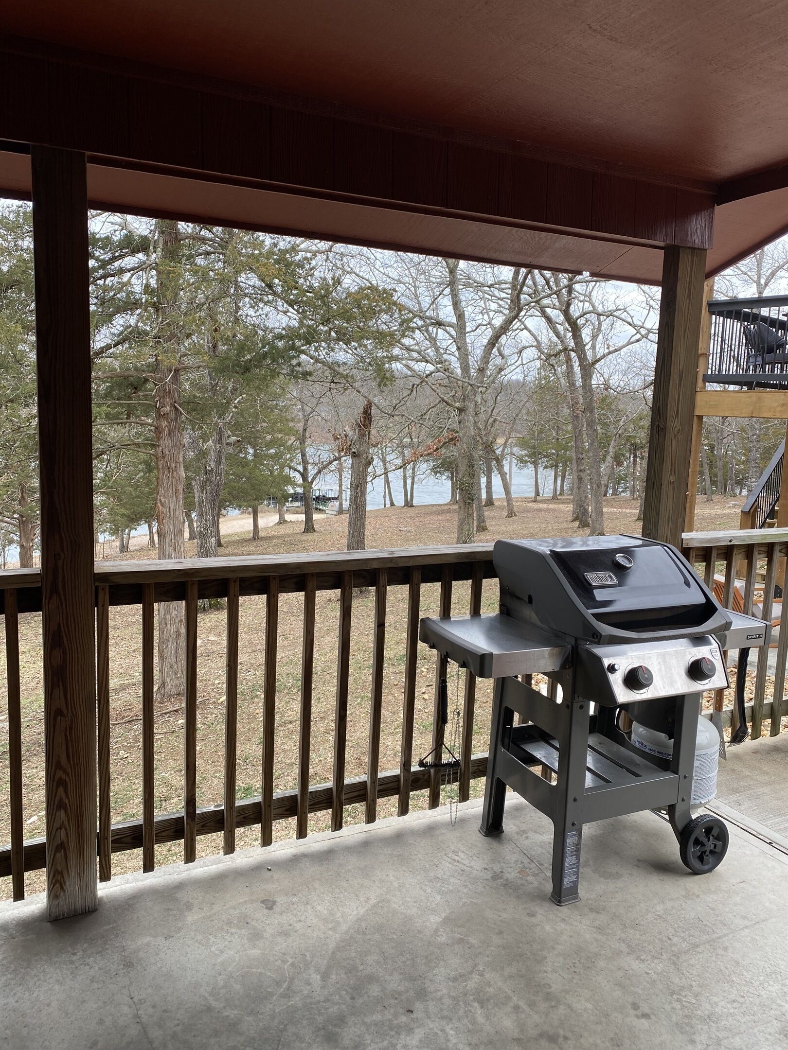 A covered outdoor area with a grill, wooden deck, and a view of trees and water.