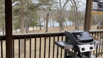 A covered outdoor area with a grill, wooden deck, and a view of trees and water.