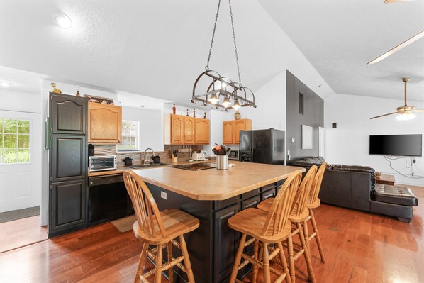 A modern kitchen with a central island, wooden chairs, and a black refrigerator.