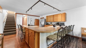 A kitchen with wooden cabinets, a central island with bar stools, a refrigerator, and a stove. - Lakefront 4BR Cabin w/ Pool + Swim & Boat dock (Kimberling City)