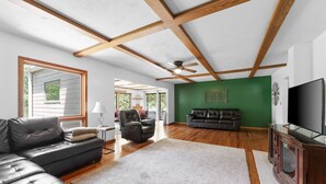 A spacious living room with a large sectional sofa, a leather armchair, and a green accent wall. - Lakefront 4BR Cabin w/ Pool + Swim & Boat dock (Kimberling City)
