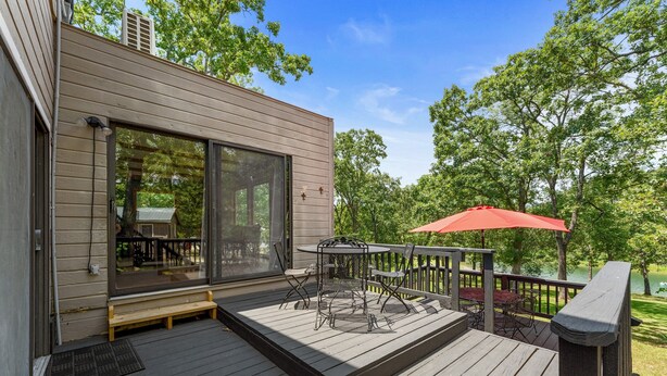 A deck with outdoor furniture and a red umbrella, overlooking a lake. - Lakefront 4BR Cabin w/ Pool + Swim & Boat dock (Kimberling City)
