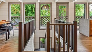 A spacious interior with a wooden deck, a dining area with chairs, and large windows offering views of greenery. - Modern A-Frame, Hot Tub, EV, 10 Guests, Dual King, 8 Mins from Downtown Hendersonville (Hendersonville)