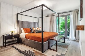 A modern bedroom with a four-poster bed, a nightstand, and a view of the outdoors.