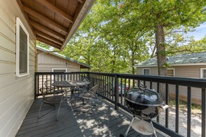 A covered outdoor deck with a table and chairs, a grill, and a view of a house and trees.