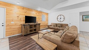 Una sala de estar con una pared de madera, un televisor, un sofá, una mesa de centro y un reloj en la pared.
