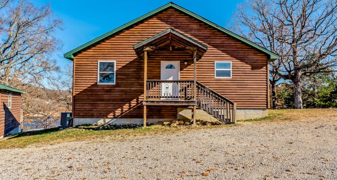 A wooden cabin with a porch, a front door, and a small staircase leading up to the entrance.