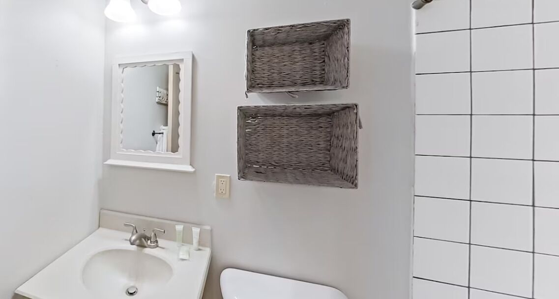 Ein Badezimmer mit weißem Waschbecken, Spiegel und zwei Korbwannen an der Wand.