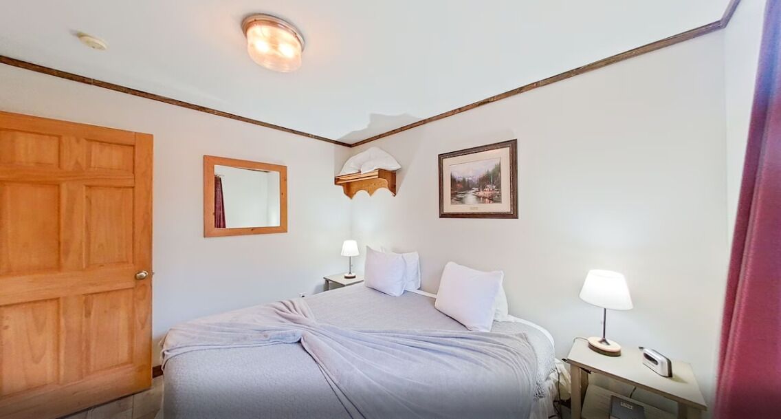 Une chambre à coucher avec un grand lit, une porte en bois, une table de chevet avec une lampe et un tableau encadré au mur.