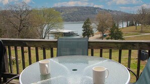 Ein Glastisch mit zwei weißen Tassen auf einer Terrasse mit Blick auf einen See und Wald.
