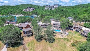 Luftaufnahme eines Wohngebiets mit Häusern, einem Swimmingpool und einer hügeligen Landschaft im Hintergrund.