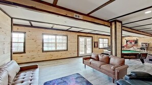 A spacious room with wooden walls, a large window, a fireplace, and a couch. - 2BR Waterfront Duplex Cabin w/ Pool + Swim & Boat dock (Branson)