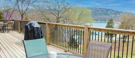 Una terraza de madera con mobiliario exterior, con vistas a un lago y colinas.