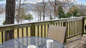 Una terraza con mesa y sillas, con vista a un cuerpo de agua y árboles.
