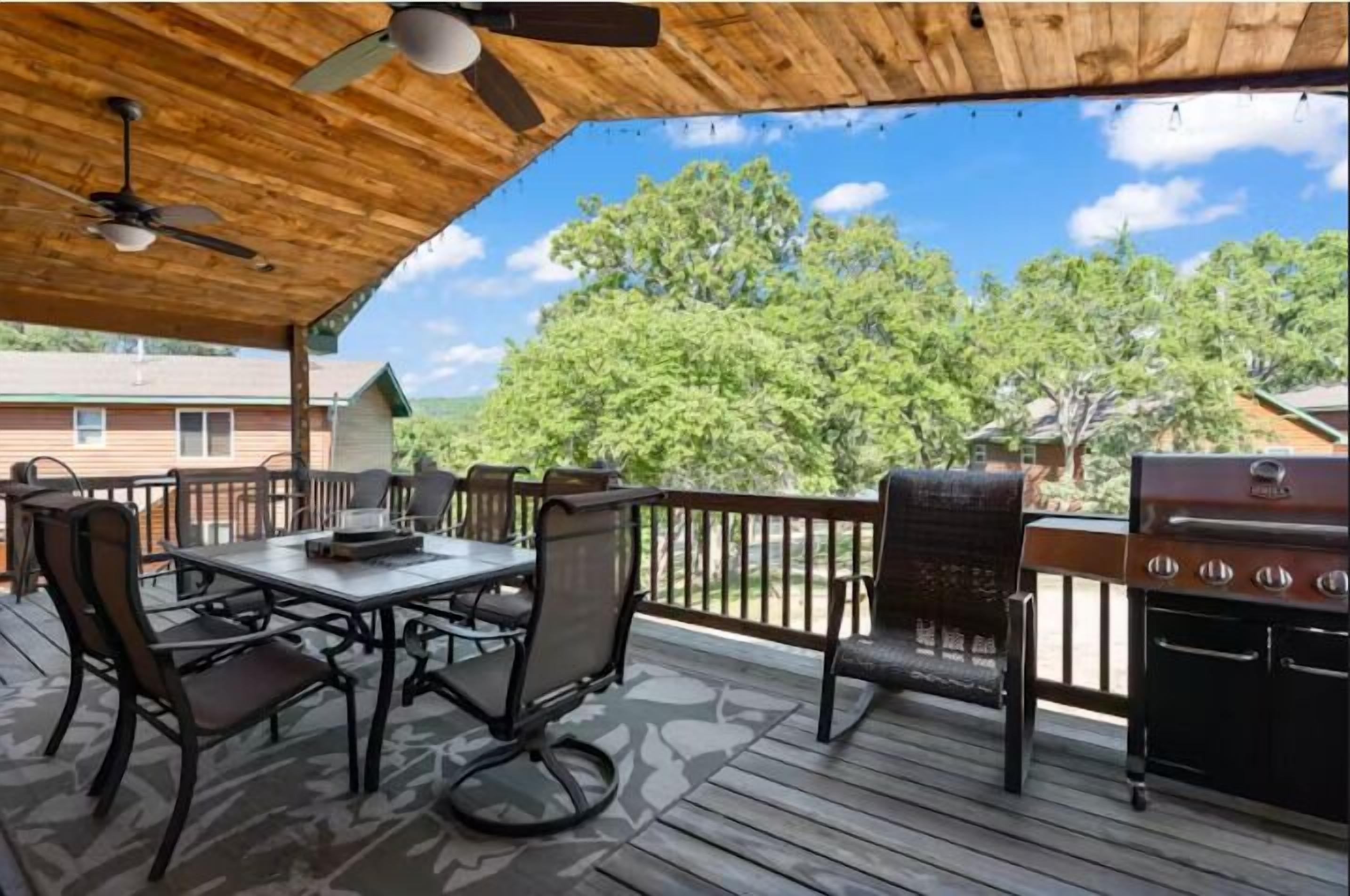 An outdoor patio with a table and chairs, a ceiling fan, and a grill.
