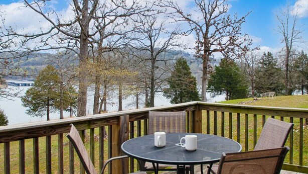 Eine Terrasse mit rundem Tisch und Stühlen, mit Blick auf einen See, Bäume und Berge im Hintergrund.