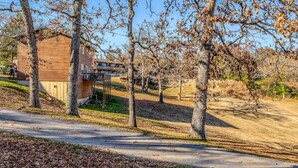 A wooden cabin with a balcony, surrounded by trees and a clear sky. - 1BR Waterfront Cabin w/ Pool + Swim & Boat dock (Branson)