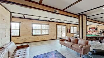 A spacious room with wooden walls and floors, a brown leather sofa, a billiards table, and a fireplace.