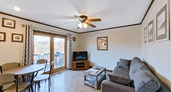 A living room with a sofa, coffee table, TV, and dining area with chairs and a table.