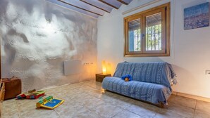 A room with a patterned sofa, a window with blinds, a wall-mounted heater, and a small table with a lamp. - Cortijo Relatillos Albox by Ruralidays (Almería)