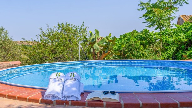 A swimming pool with two towels and sunglasses on the edge, surrounded by greenery. - Cortijo Relatillos Albox by Ruralidays (Almería)