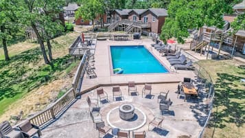 A swimming pool with lounge chairs and a fire pit, surrounded by wooden deck and trees.