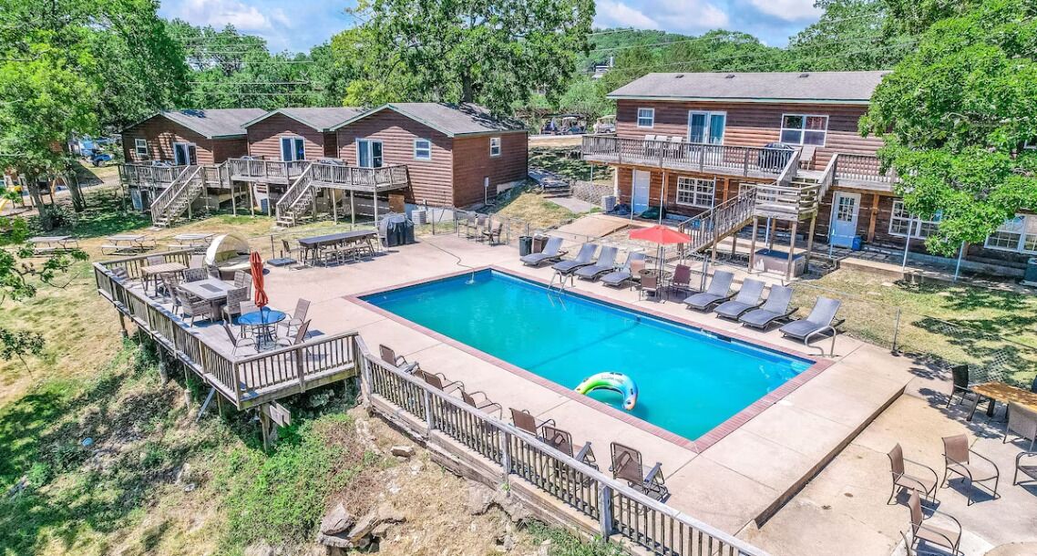 Un espace piscine comprenant des chaises longues, un jacuzzi et une terrasse avec des escaliers menant à un bâtiment.