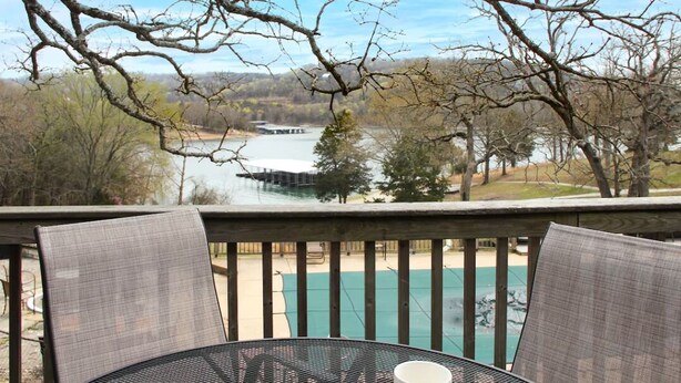 Une terrasse avec une table et des chaises donnant sur une piscine et un lac.