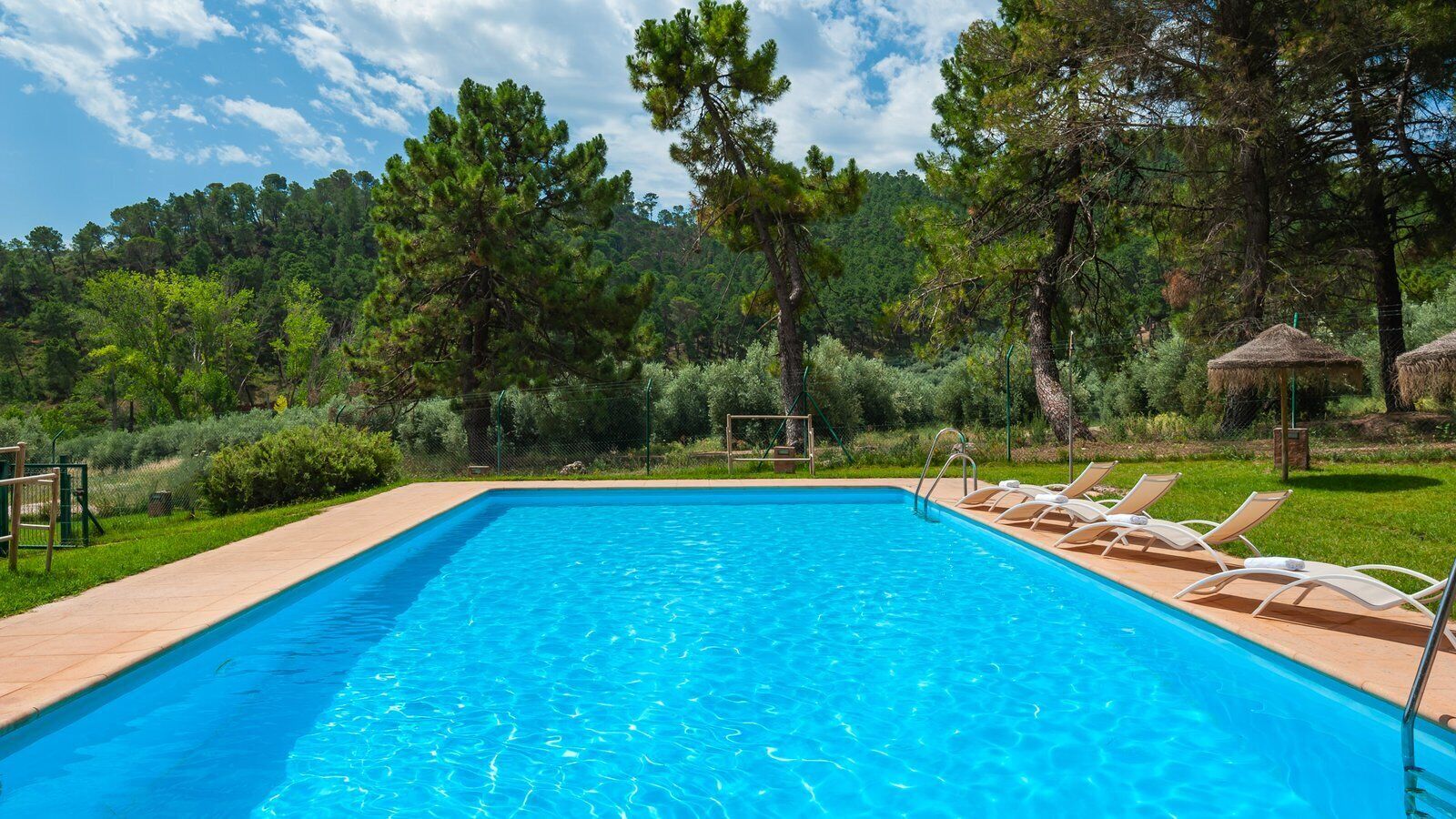 A rectangular swimming pool with clear blue water, surrounded by a wooden deck and lounge chairs.
