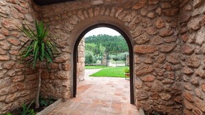 A stone archway leading to a paved patio with a view of a green landscape and a fence. - Valdemarín Rural Cortijos Nuevos by Ruralidays (Jaén)