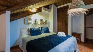 A bedroom with a bed, pillows, a bedside table, a hanging light fixture, and a wooden door. - Valdemarín Rural Cortijos Nuevos by Ruralidays (Jaén)