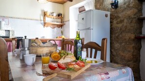 Une table dressée pour le petit-déjeuner avec du pain, des tomates, une bouteille d’huile d’olive et une machine à café.