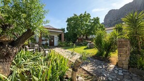 Une maison avec un chemin de pierre menant à un patio, entourée d’une végétation luxuriante et avec une chaîne de montagnes en toile de fond.