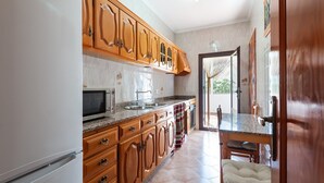 A kitchen with wooden cabinets, a microwave, a sink, and a dining area with a table and chairs.